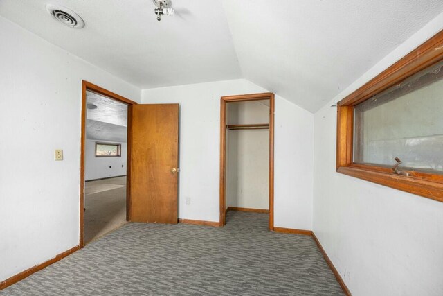 unfurnished bedroom with visible vents, baseboards, a closet, carpet floors, and lofted ceiling