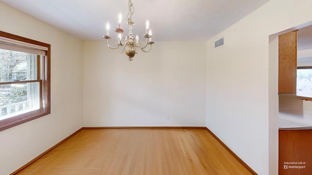 empty room featuring light wood finished floors, visible vents, baseboards, and an inviting chandelier