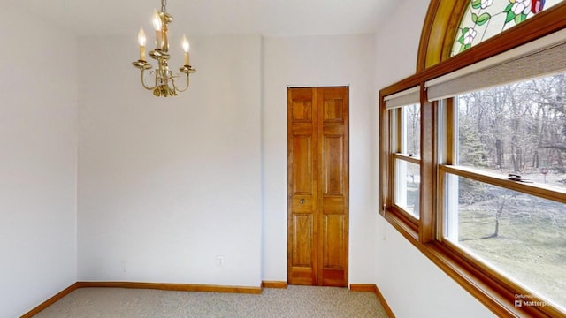 carpeted spare room with an inviting chandelier, baseboards, and plenty of natural light