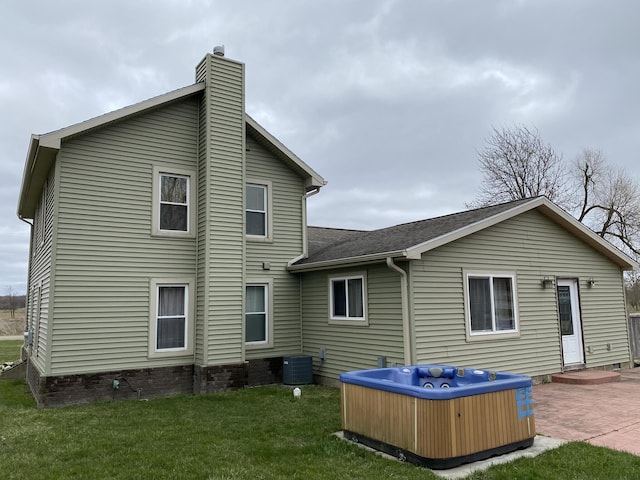 back of property with a chimney, a patio area, central AC, a hot tub, and a yard