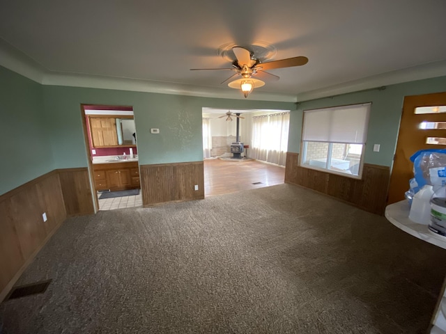 unfurnished living room featuring wood walls, carpet floors, a wainscoted wall, and ceiling fan