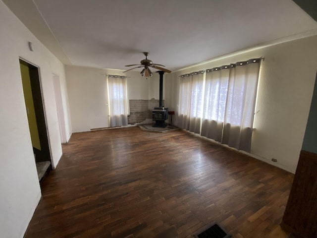 unfurnished room with wood finished floors, a wood stove, a ceiling fan, and visible vents