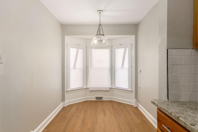 unfurnished dining area with visible vents, baseboards, light wood-type flooring, and a chandelier