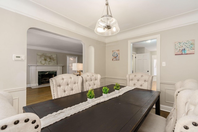 dining area featuring arched walkways, wood finished floors, a fireplace, and a wainscoted wall