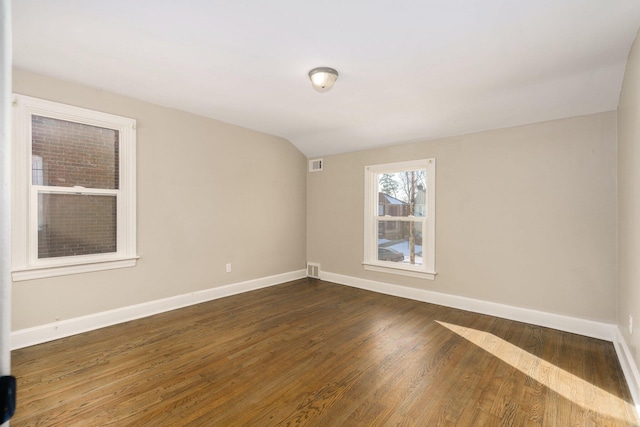 empty room with visible vents, baseboards, vaulted ceiling, and dark wood finished floors