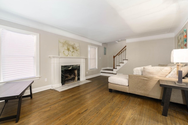 living room featuring baseboards, ornamental molding, a fireplace, stairs, and wood finished floors