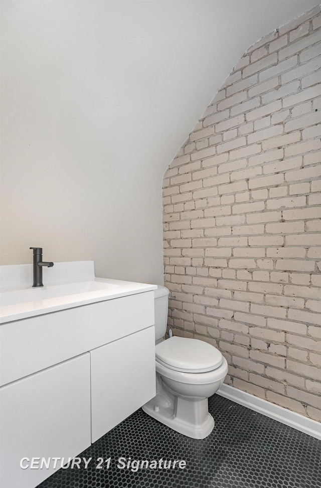 105 Parkwood Ct, Bay City, MI 48706 - bathroom featuring vanity, vaulted ceiling, toilet, tile patterned floors, and brick wall