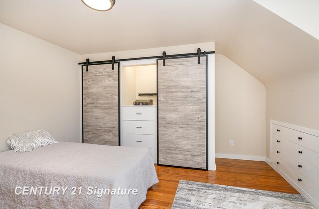 105 Parkwood Ct, Bay City, MI 48706 - bedroom with baseboards, light wood finished floors, a barn door, and vaulted ceiling