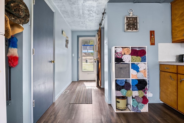 corridor with a barn door, dark wood-type flooring, visible vents, and baseboards