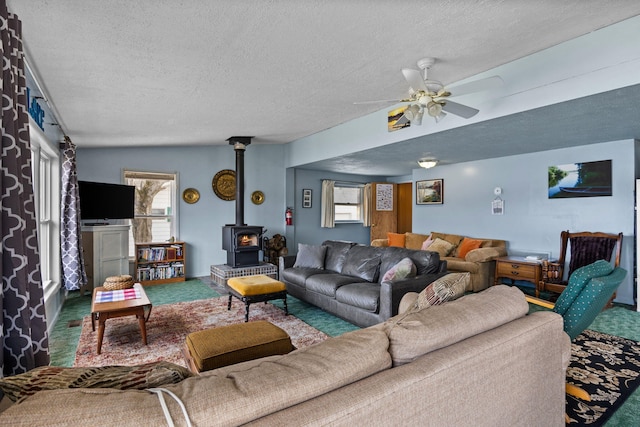 living room featuring carpet floors, a wood stove, ceiling fan, and a textured ceiling