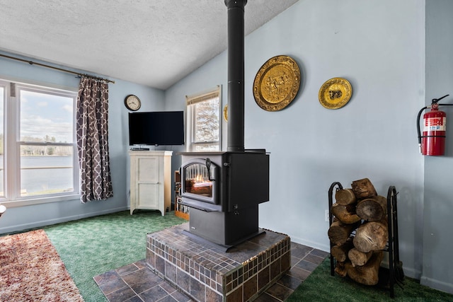 living area with baseboards, dark colored carpet, a wood stove, a textured ceiling, and vaulted ceiling