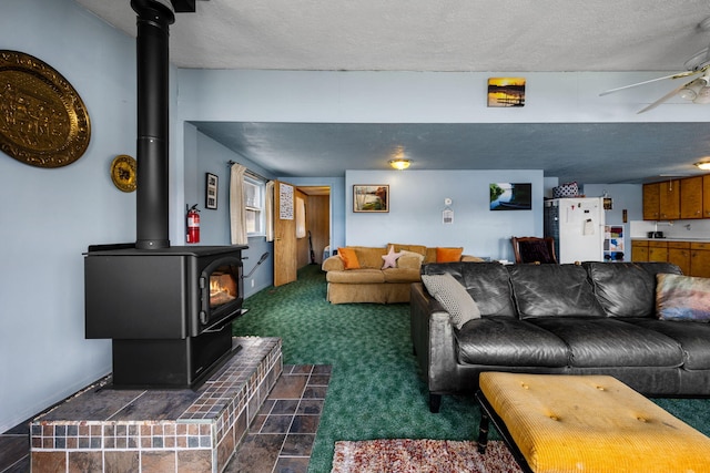 living room with ceiling fan, a wood stove, dark colored carpet, and a textured ceiling
