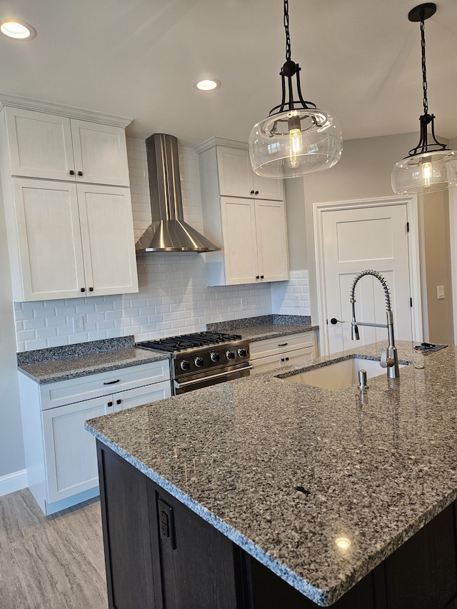 kitchen featuring white cabinetry, backsplash, wall chimney exhaust hood, a sink, and high end stove