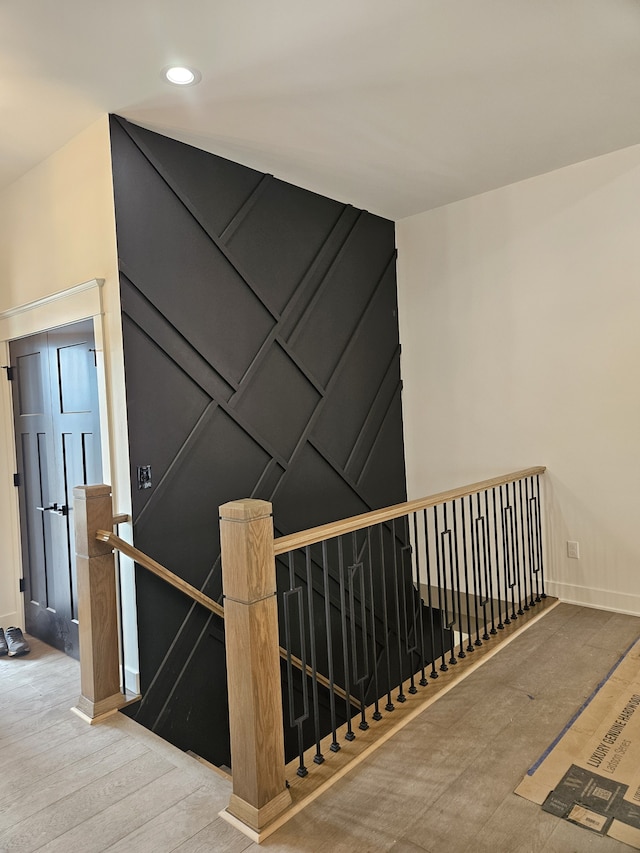 stairway featuring a decorative wall, wood finished floors, baseboards, and recessed lighting
