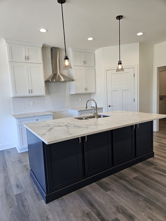 kitchen with a sink, white cabinetry, wall chimney exhaust hood, and a large island with sink