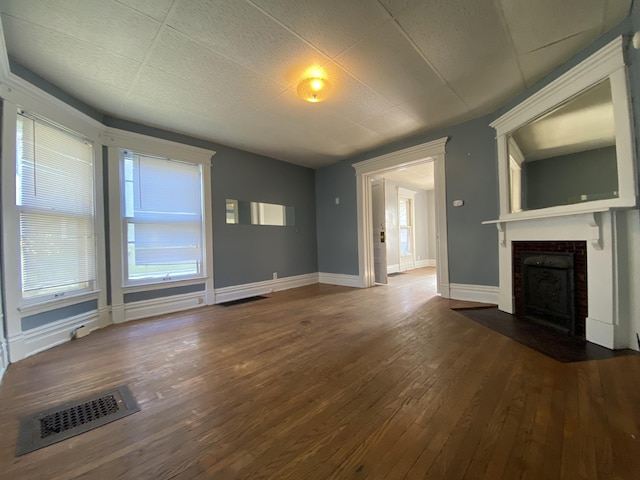 unfurnished living room with a fireplace with flush hearth, visible vents, baseboards, and hardwood / wood-style floors