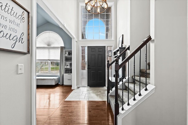 entrance foyer with lofted ceiling, stairway, wood finished floors, and a notable chandelier