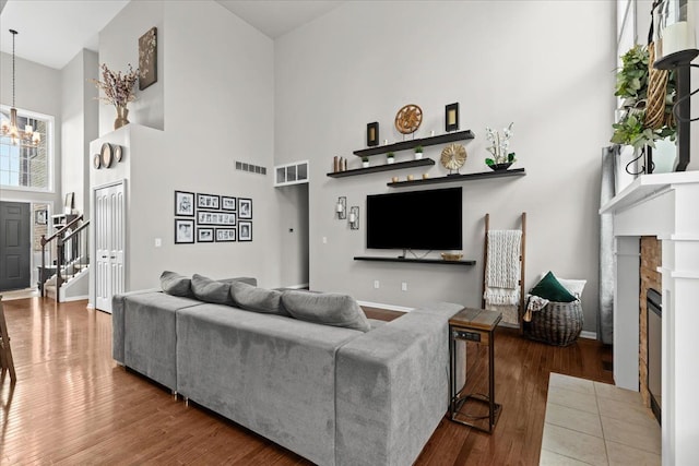 living area featuring wood finished floors, a brick fireplace, visible vents, a notable chandelier, and a towering ceiling