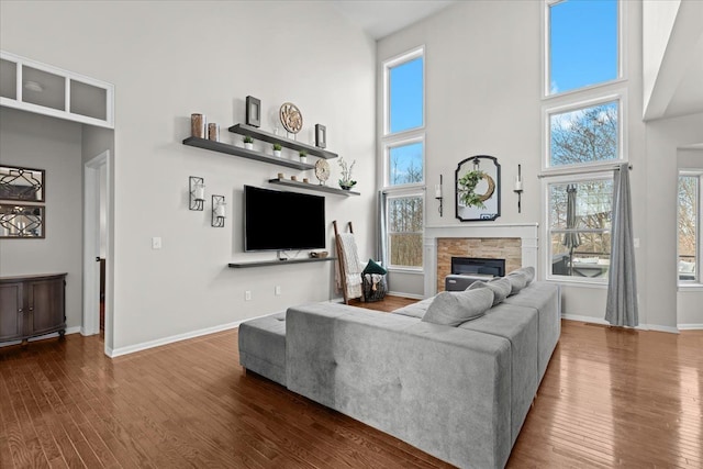 living area with a fireplace, baseboards, dark wood-style floors, and a high ceiling