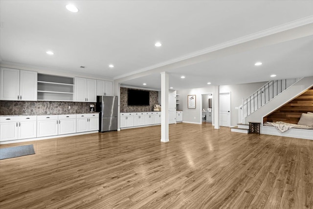 unfurnished living room with crown molding, stairway, light wood-style floors, baseboards, and recessed lighting