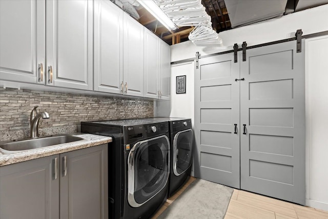 clothes washing area with washing machine and dryer, a sink, cabinet space, and a barn door