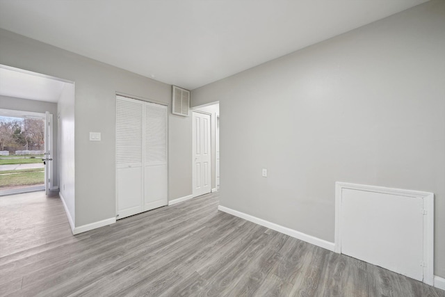unfurnished bedroom featuring visible vents, baseboards, a closet, and wood finished floors