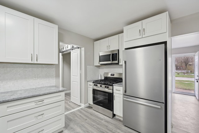 kitchen with light wood-style flooring, tasteful backsplash, white cabinets, light stone counters, and stainless steel appliances