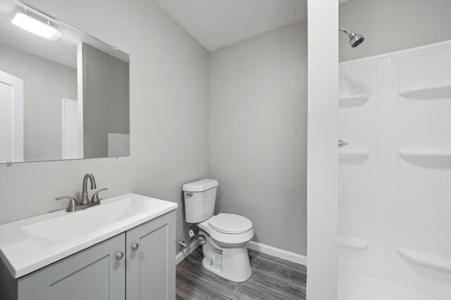 bathroom featuring vanity, toilet, wood finished floors, walk in shower, and baseboards