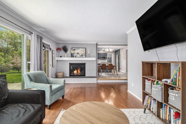 living area featuring ornamental molding, a chandelier, wood finished floors, a fireplace, and baseboards