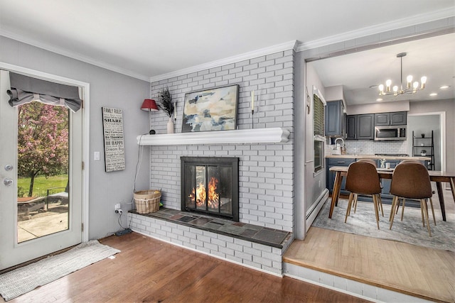 living area featuring wood finished floors, a fireplace, baseboard heating, a chandelier, and ornamental molding