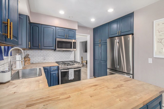 kitchen with appliances with stainless steel finishes, blue cabinets, a sink, tasteful backsplash, and wood counters
