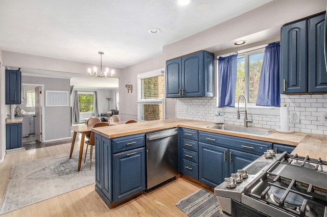 kitchen with appliances with stainless steel finishes, blue cabinetry, a sink, a peninsula, and a chandelier