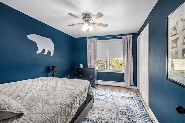 bedroom featuring a baseboard heating unit, baseboards, wood finished floors, and ceiling fan