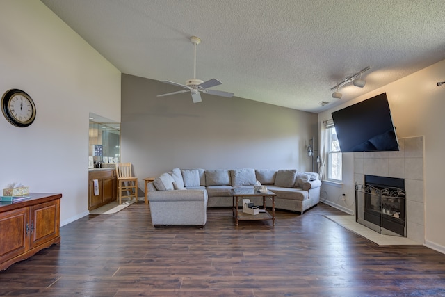 living room featuring a ceiling fan, a textured ceiling, a tiled fireplace, rail lighting, and dark wood-type flooring
