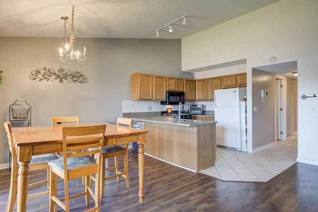 kitchen with a peninsula, freestanding refrigerator, black microwave, track lighting, and high vaulted ceiling