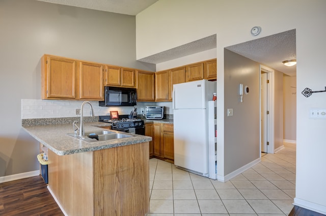 kitchen with a sink, baseboards, black appliances, a peninsula, and tasteful backsplash