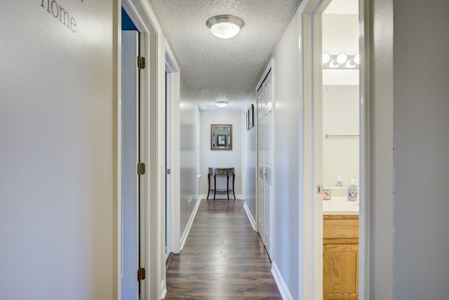 corridor with dark wood-type flooring, a textured ceiling, and baseboards