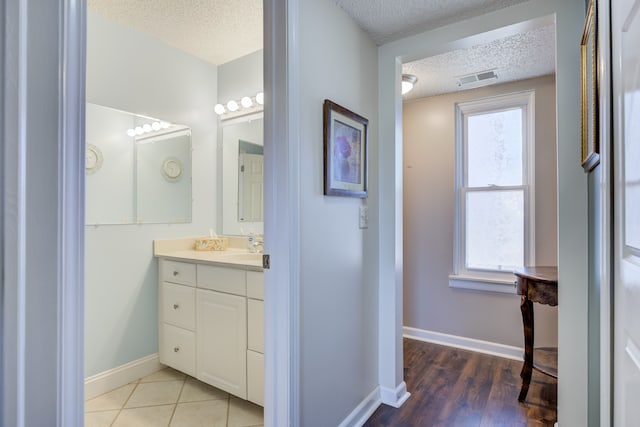 bathroom with baseboards, visible vents, a textured ceiling, and a healthy amount of sunlight