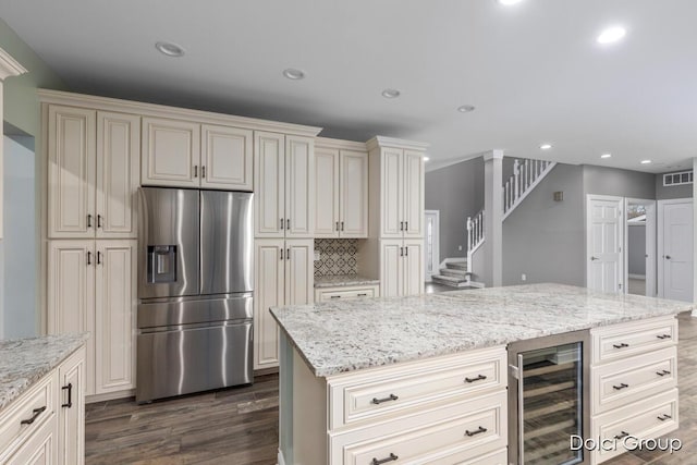 kitchen featuring stainless steel fridge with ice dispenser, visible vents, light stone counters, dark wood-style flooring, and beverage cooler