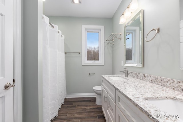 full bathroom featuring toilet, wood finished floors, a sink, double vanity, and baseboards