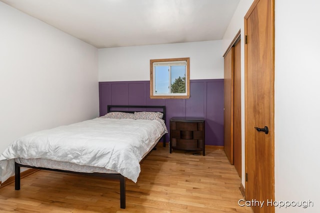 bedroom with a closet, light wood-type flooring, and a wainscoted wall