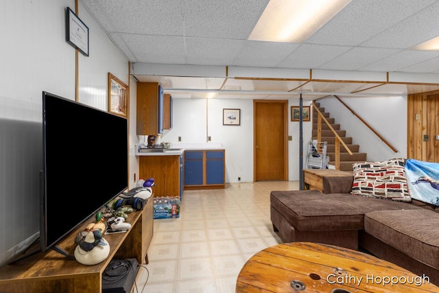 living room with a paneled ceiling, light floors, and stairs