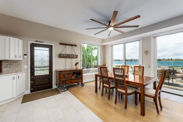 dining room with a ceiling fan, light wood-style floors, and a water view