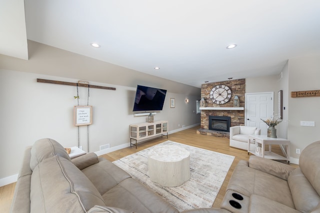 living room featuring wood finished floors, visible vents, and a stone fireplace