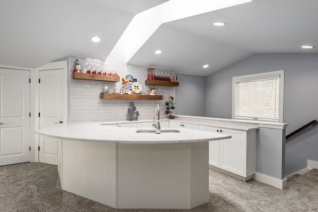 kitchen featuring a peninsula, light carpet, a sink, and vaulted ceiling