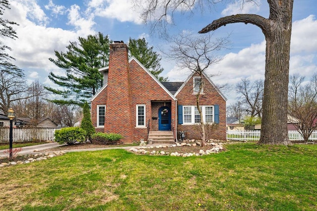 tudor-style house featuring a front yard, brick siding, fence, and a chimney