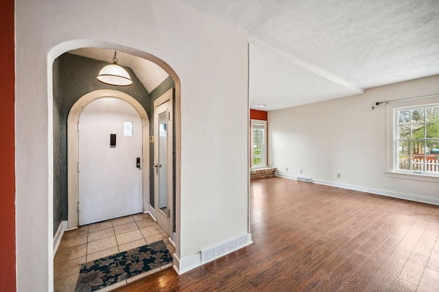 foyer entrance with arched walkways, wood finished floors, visible vents, and a textured ceiling