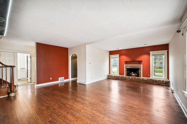 unfurnished living room with a fireplace, stairway, visible vents, and hardwood / wood-style flooring
