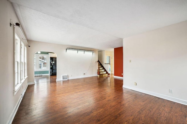 unfurnished living room with visible vents, baseboards, arched walkways, wood finished floors, and stairs