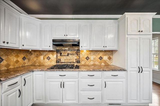 kitchen featuring white cabinets, under cabinet range hood, dark stone countertops, and gas cooktop